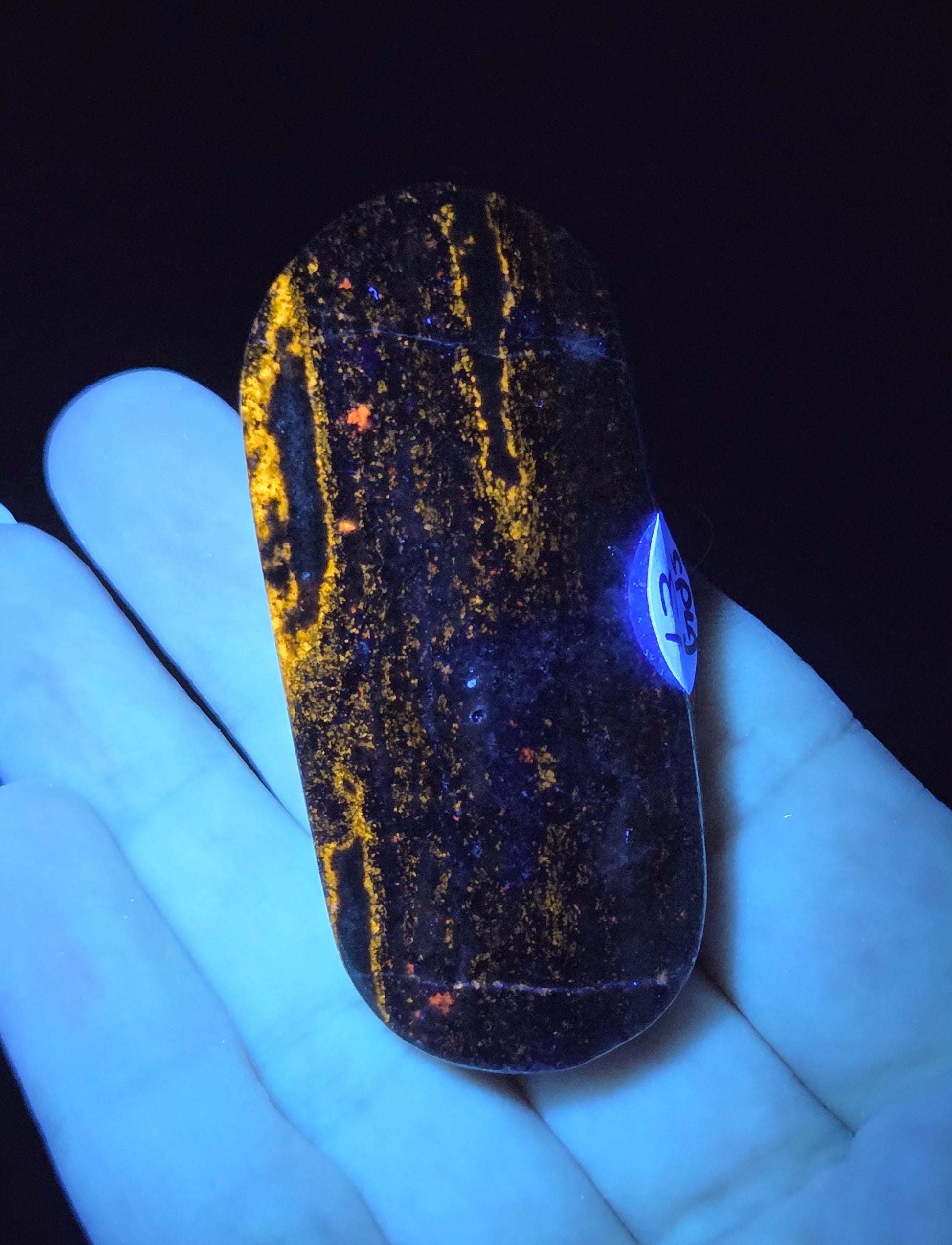 Hand holding a glowing stone with yellow specks under a black light