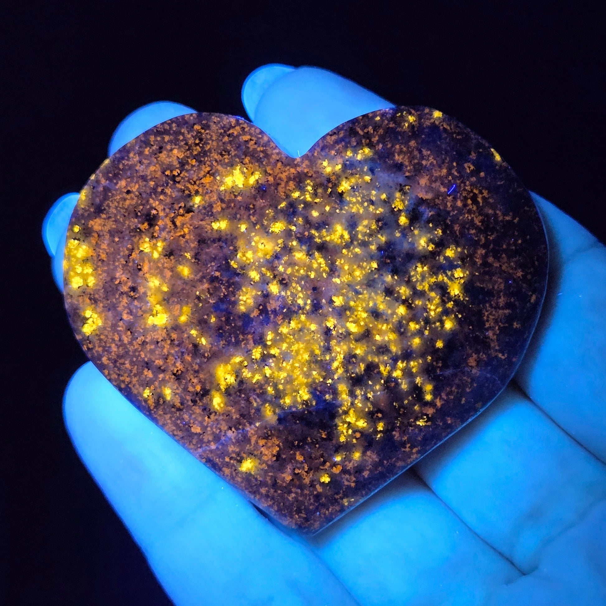 Heart-shaped object glowing yellow under a black light held in a hand.