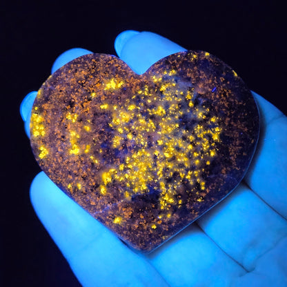 Heart-shaped object glowing yellow under a black light held in a hand.