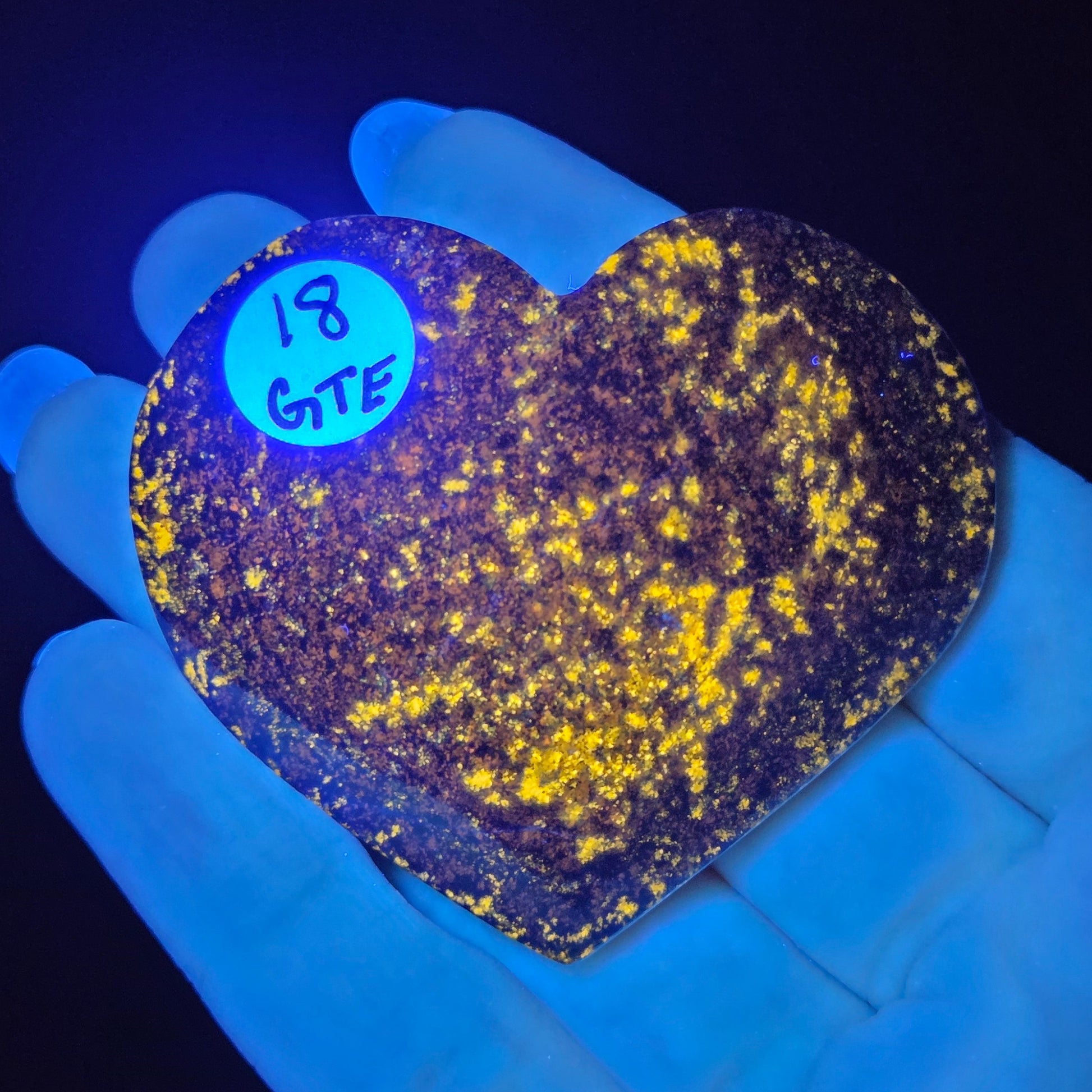 Heart-shaped object with yellow speckles under black light, held by a gloved hand.