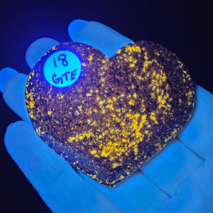 Heart-shaped object with yellow speckles under black light, held by a gloved hand.