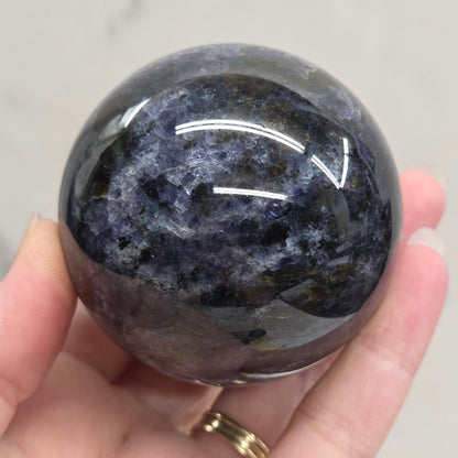 Hand holding a dark stone sphere against a neutral background
