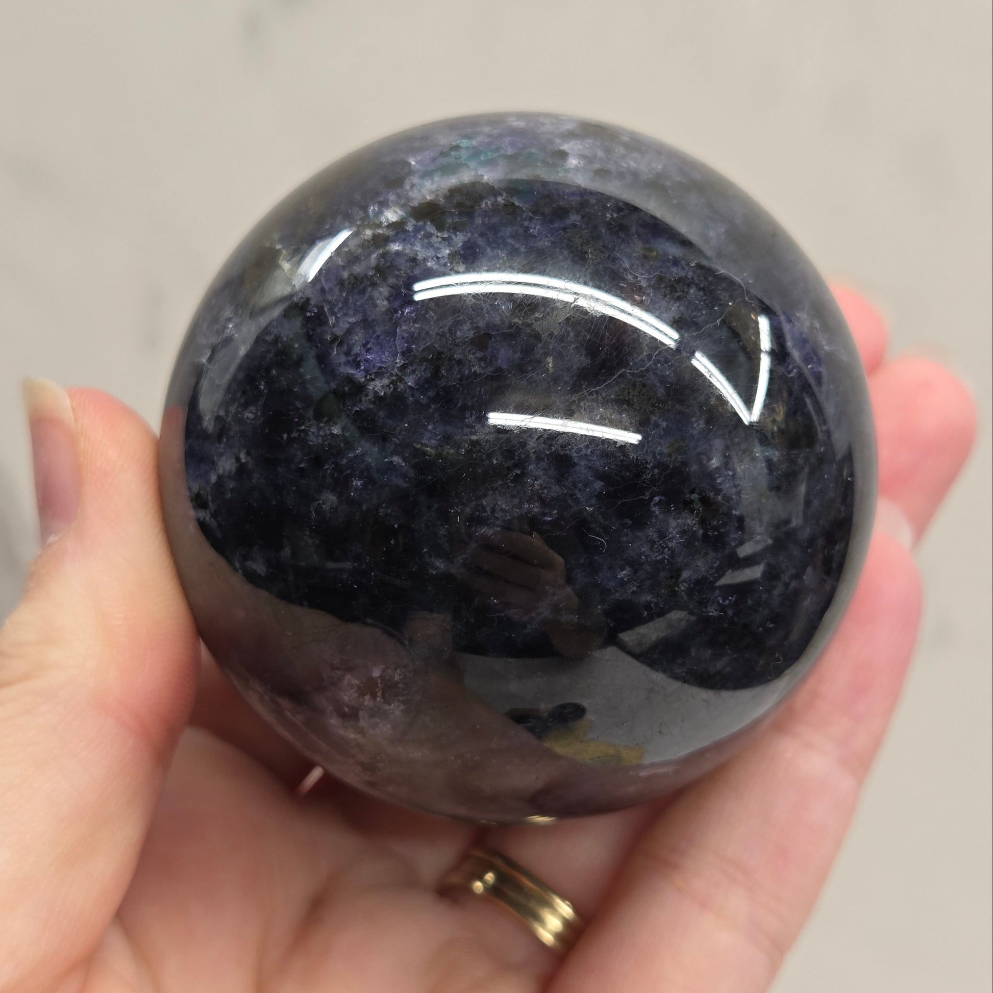 Hand holding a dark purple crystal ball against a neutral background
