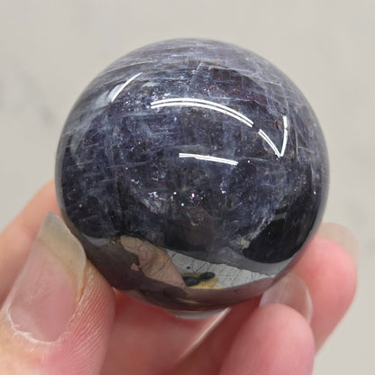Hand holding a dark blue stone against a neutral background