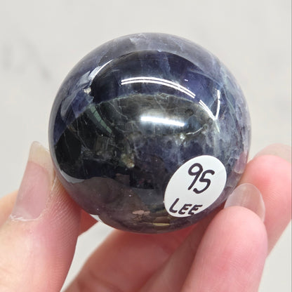 Hand holding a dark blue stone with a visible number label against a light gray background