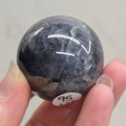 Hand holding a dark blue crystal ball with a visible label on a light gray background