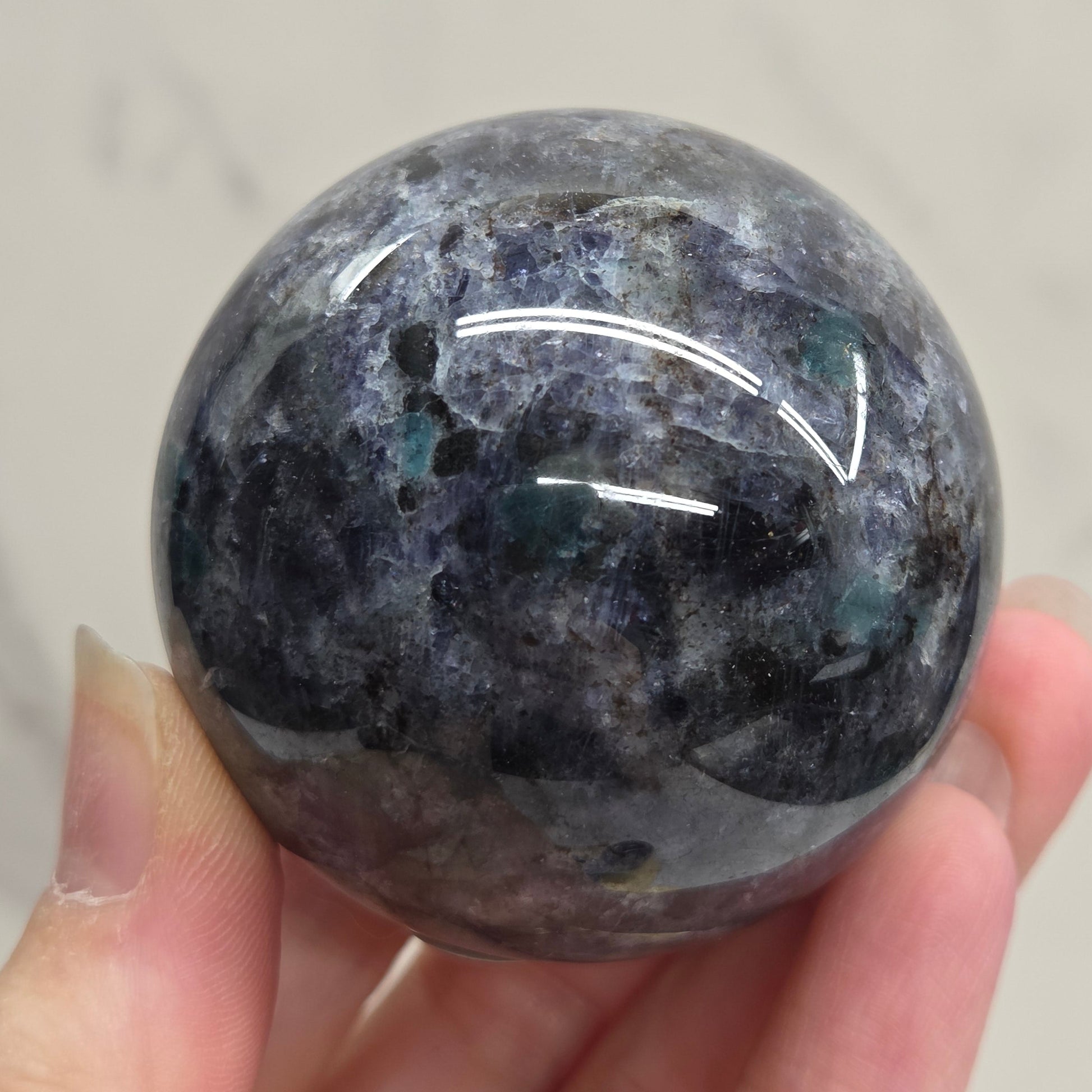 Hand holding a polished dark stone with a subtle pattern against a neutral background