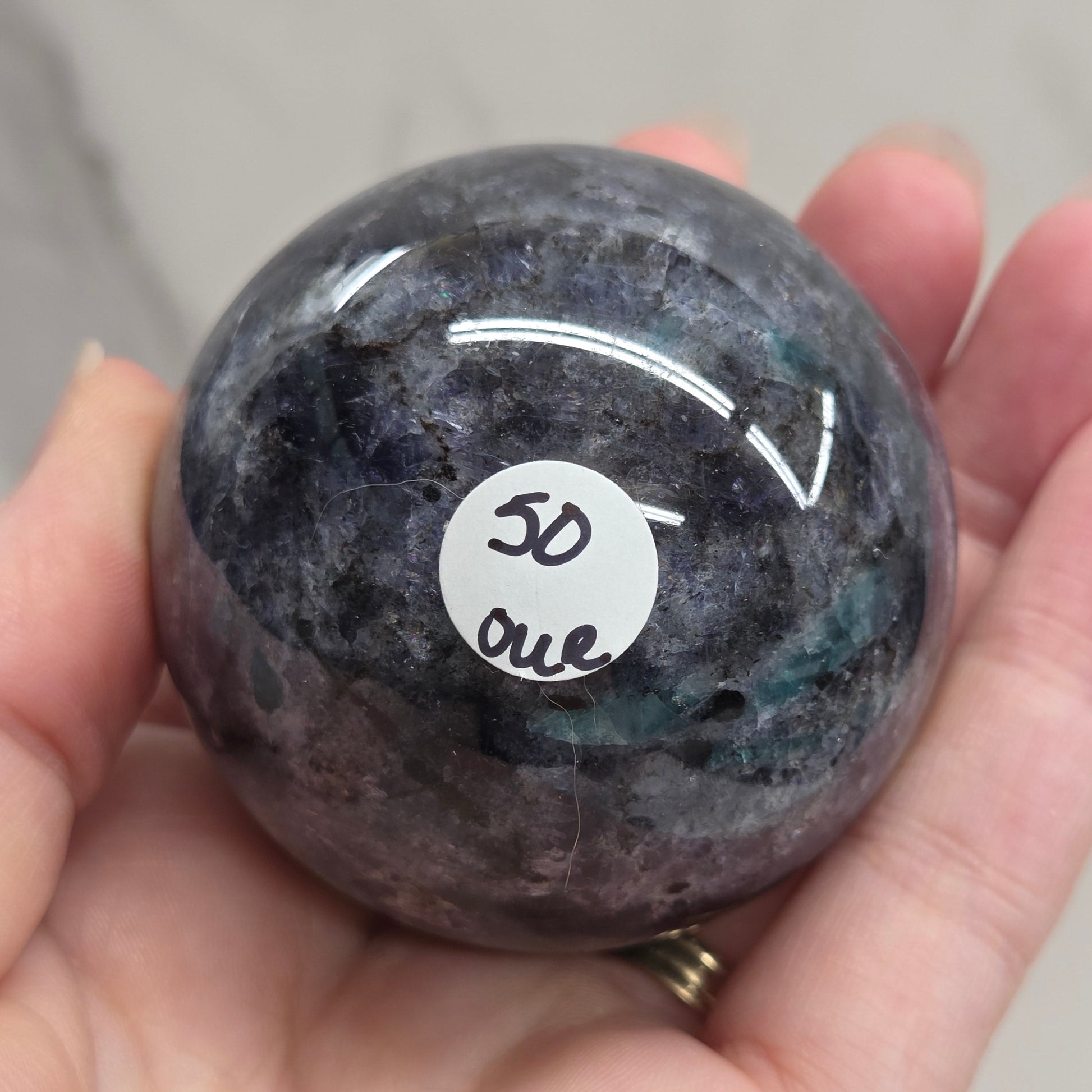 Hand holding a purple stone with a white label featuring text and symbols.
