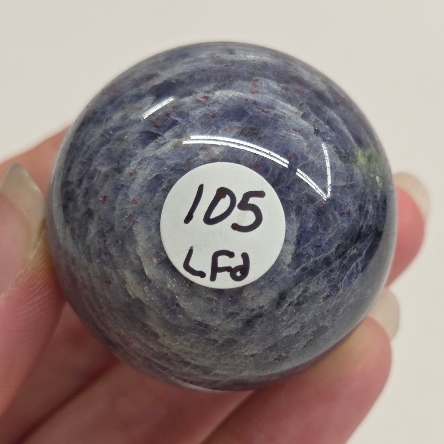 Hand holding a blue stone with a white label on a plain background