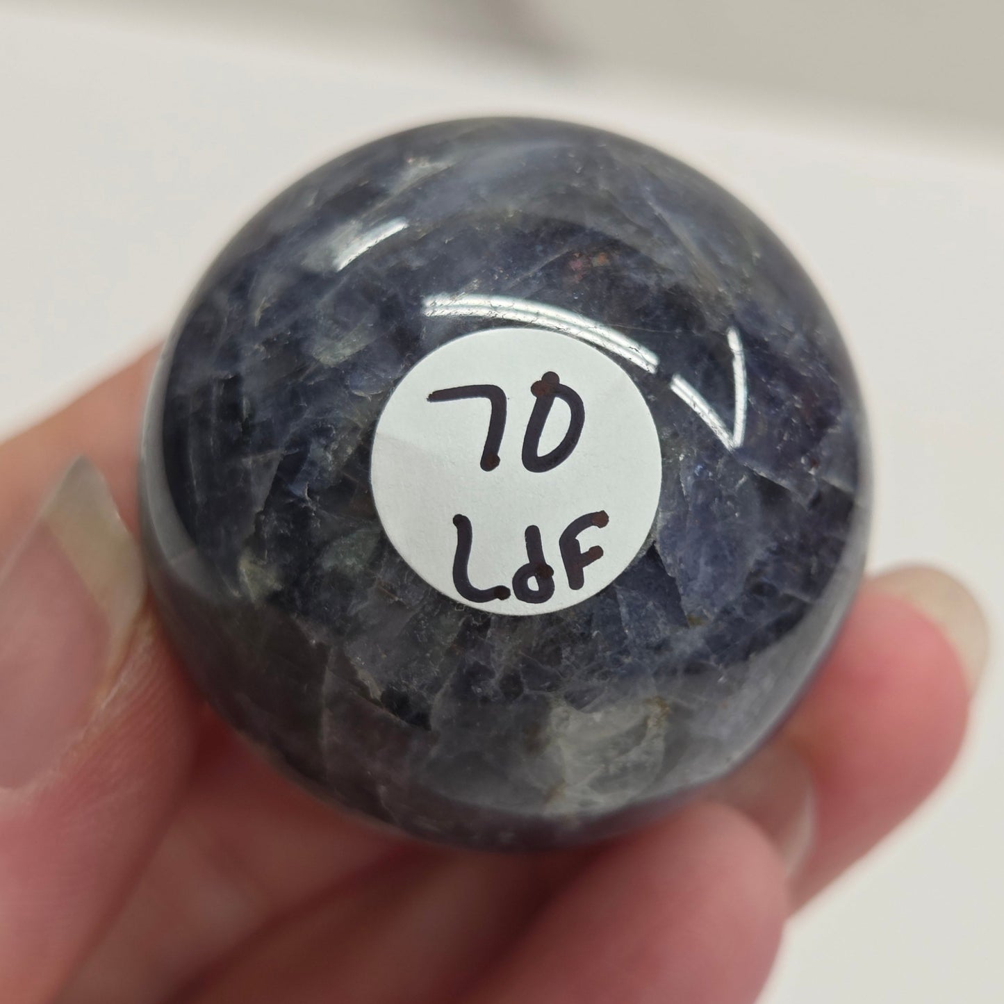 Hand holding a dark blue stone with a white label featuring text on a plain background