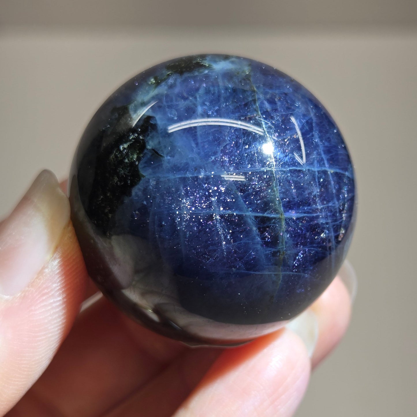 Hand holding a blue starry sphere against a neutral background