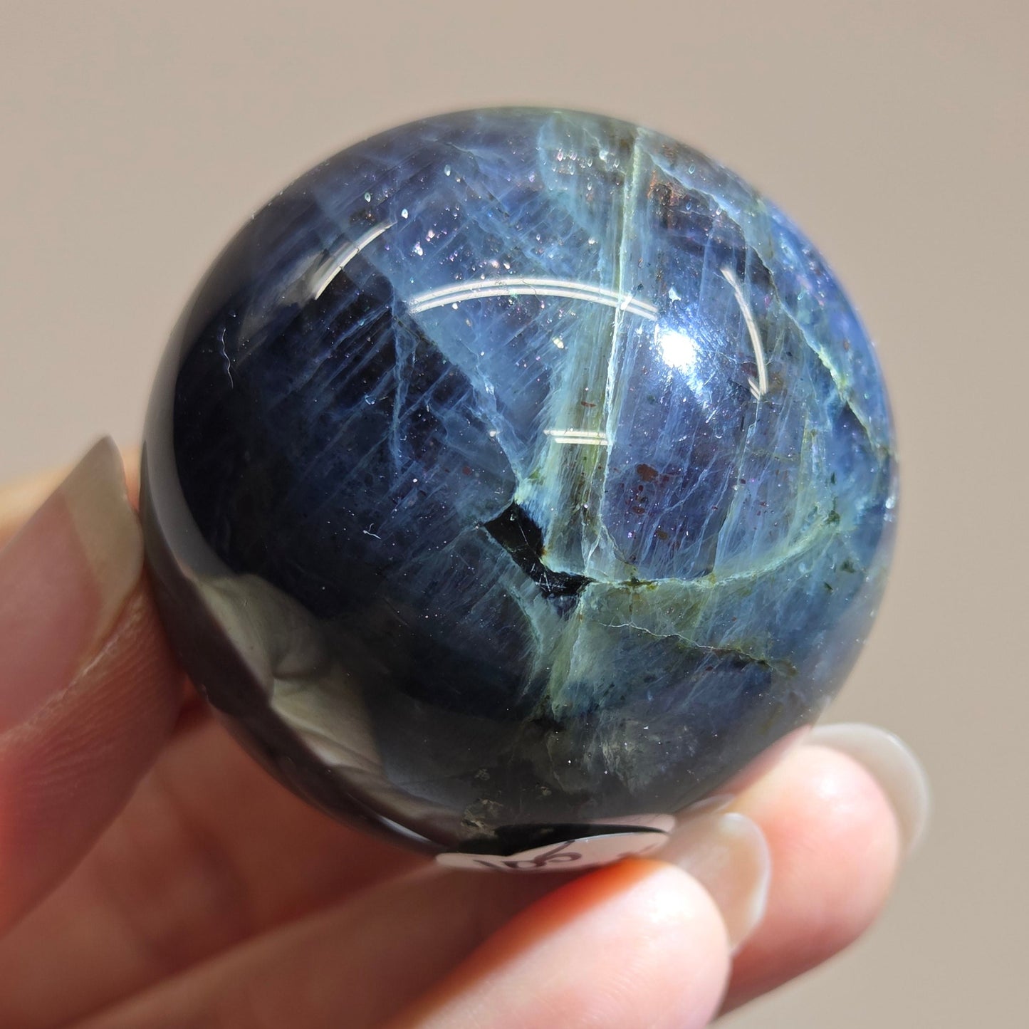 Hand holding a blue crystal ball against a neutral background
