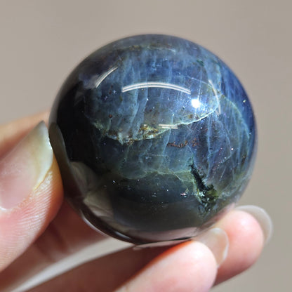 Hand holding a dark blue crystal ball against a neutral background