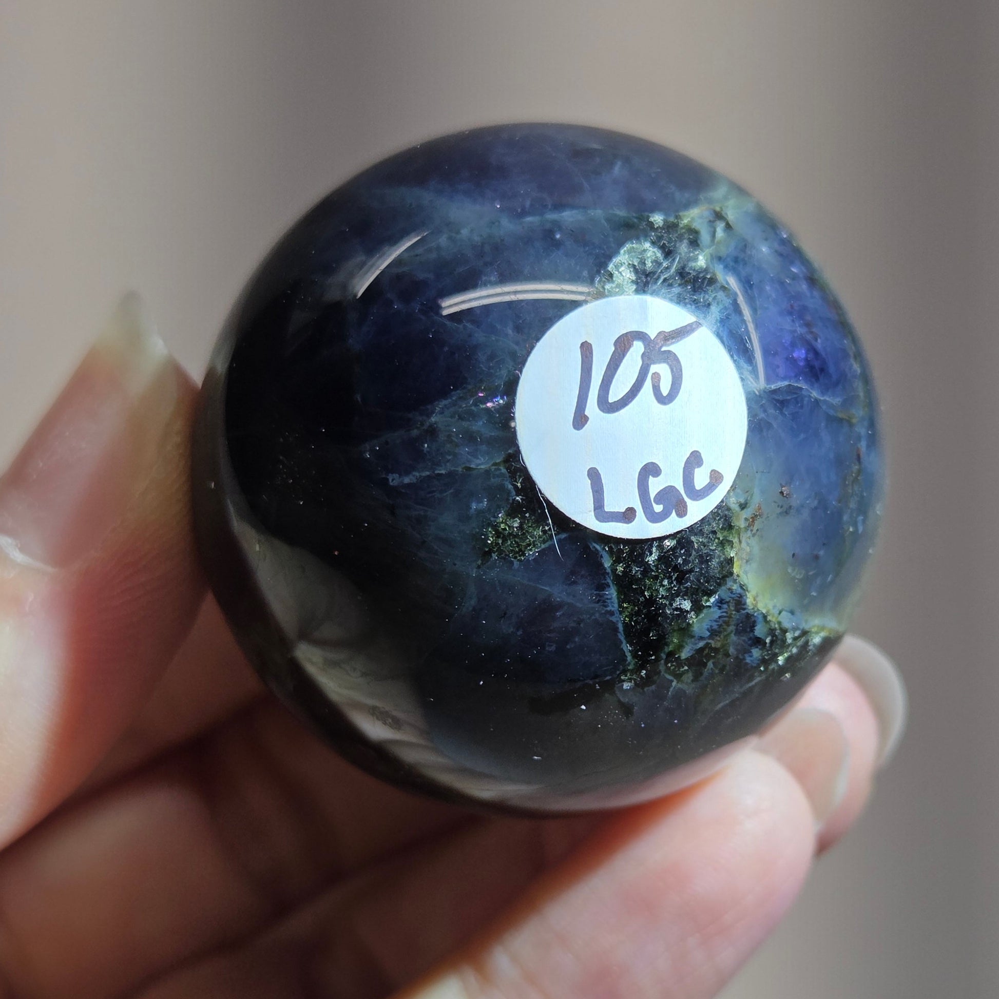 Hand holding a dark blue marbled object with a label on a neutral background