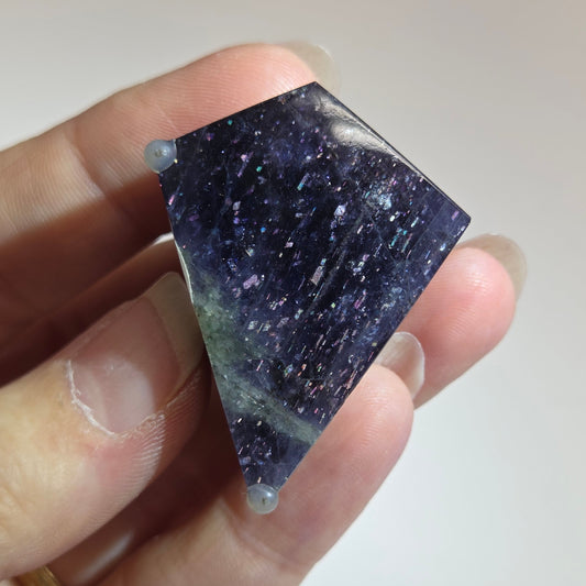 Hand holding a dark purple crystal against a plain background