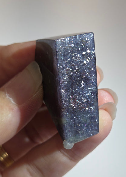 Hand holding a rectangular crystal with a glittery surface against a plain background