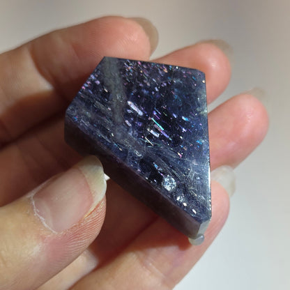 Hand holding a rough purple stone against a neutral background