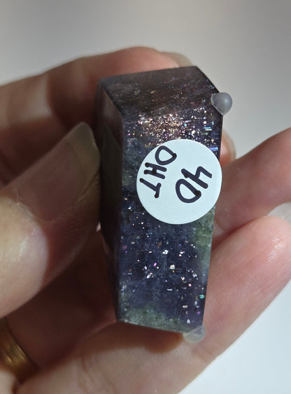 Hand holding a small, rectangular crystal with '40 DHT' label against a neutral background