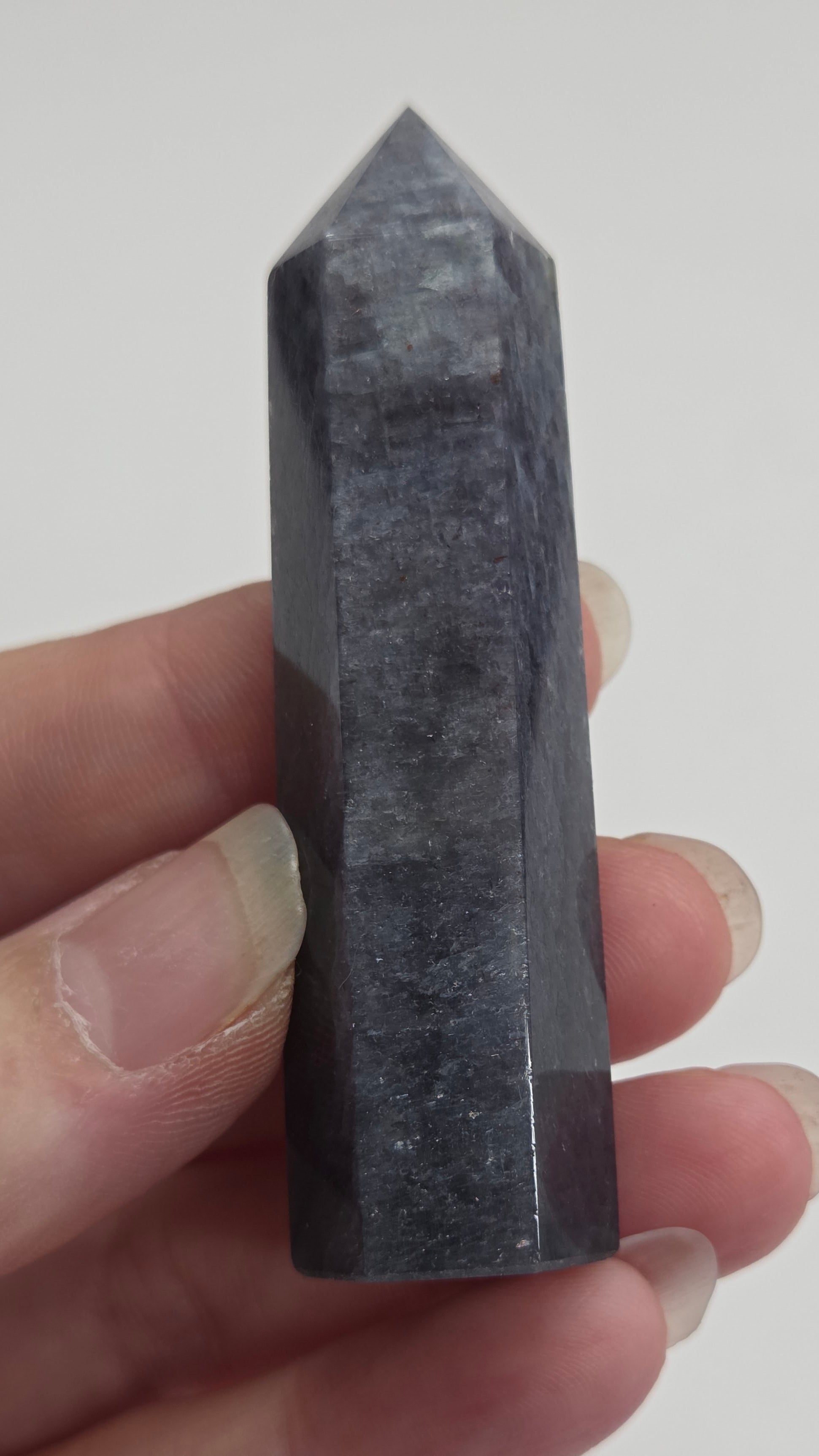 Hand holding a dark crystal pyramid against a plain background
