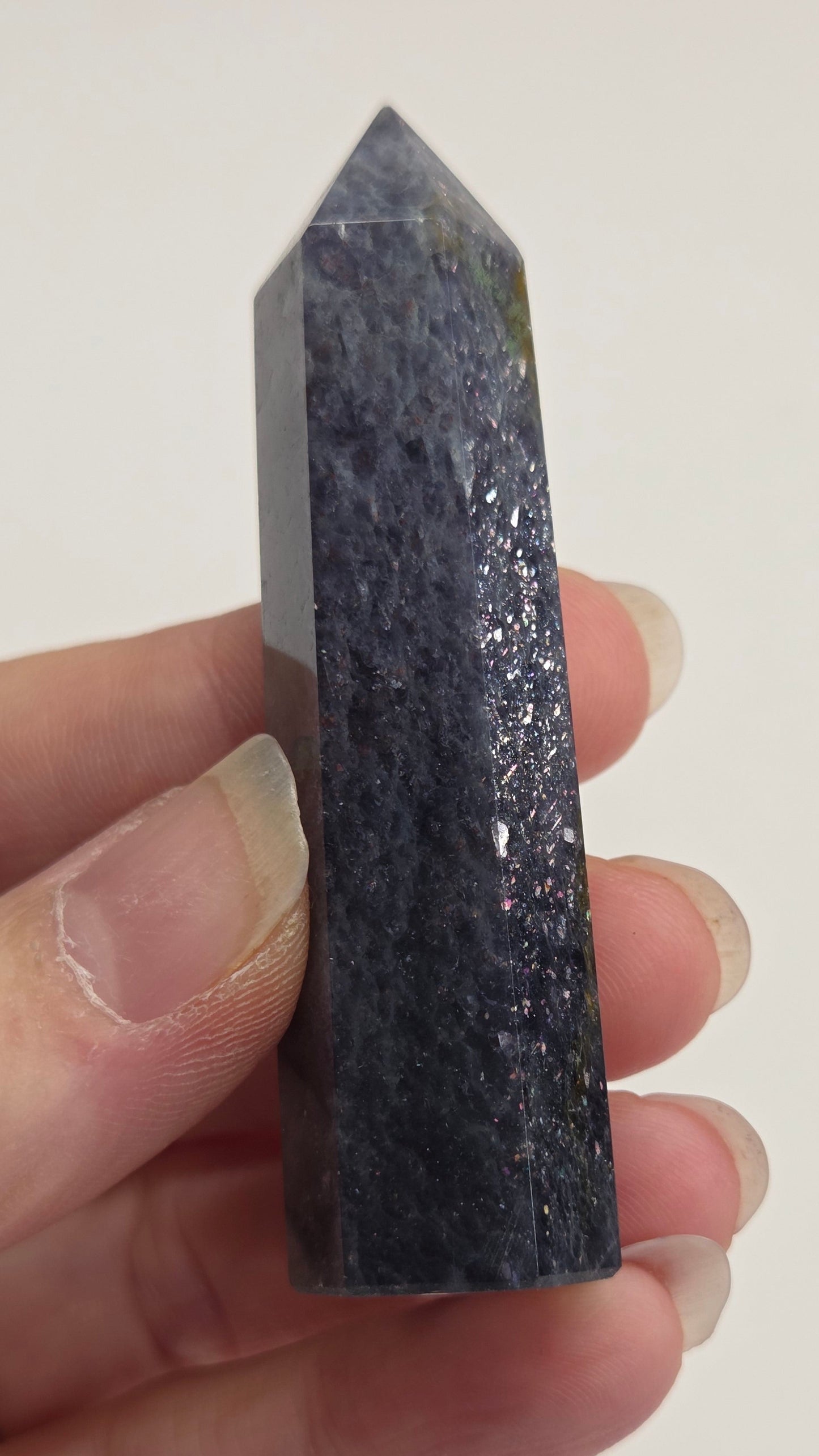 Hand holding a dark purple crystal against a white background