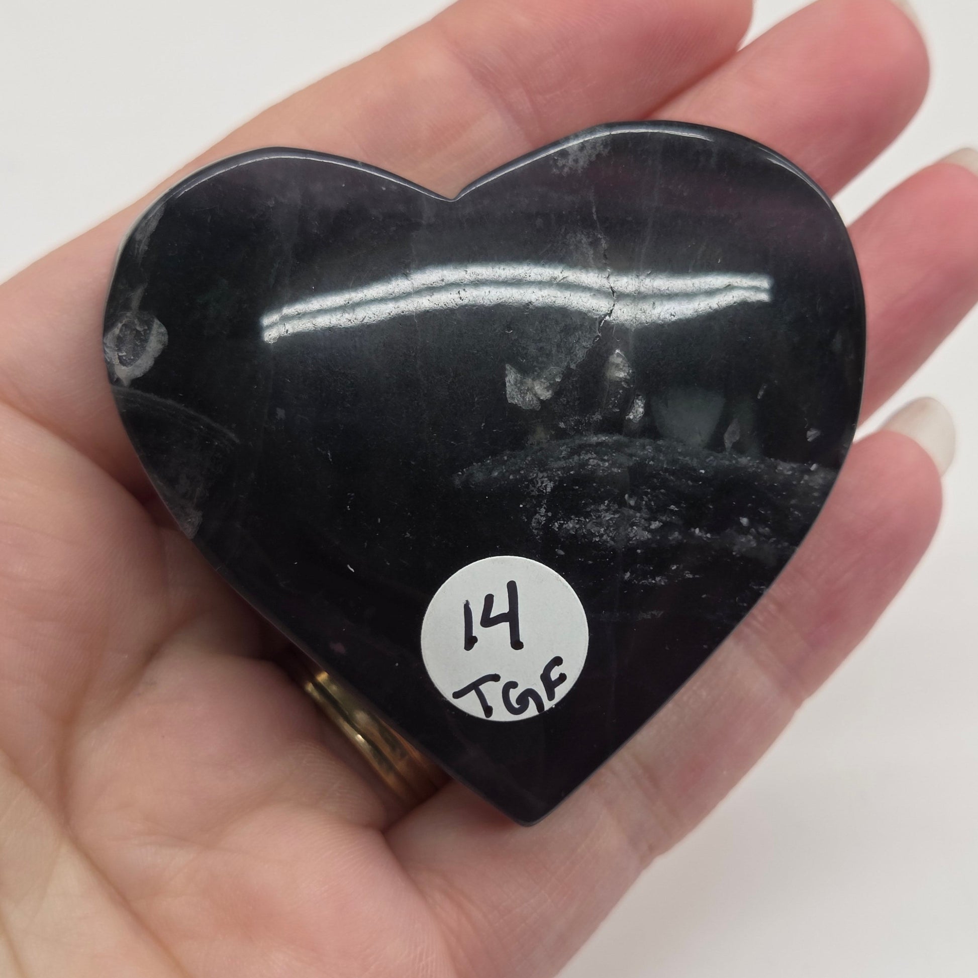 Heart-shaped black stone held in a hand with a white background