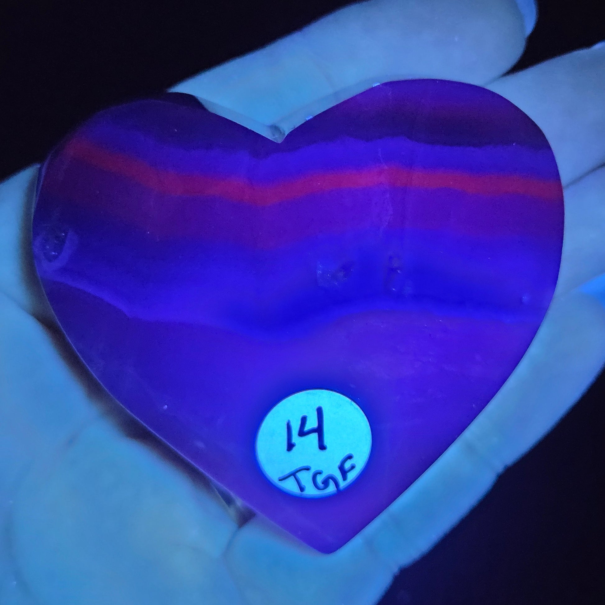 Purple crystal stone with a label on a hand against a dark background