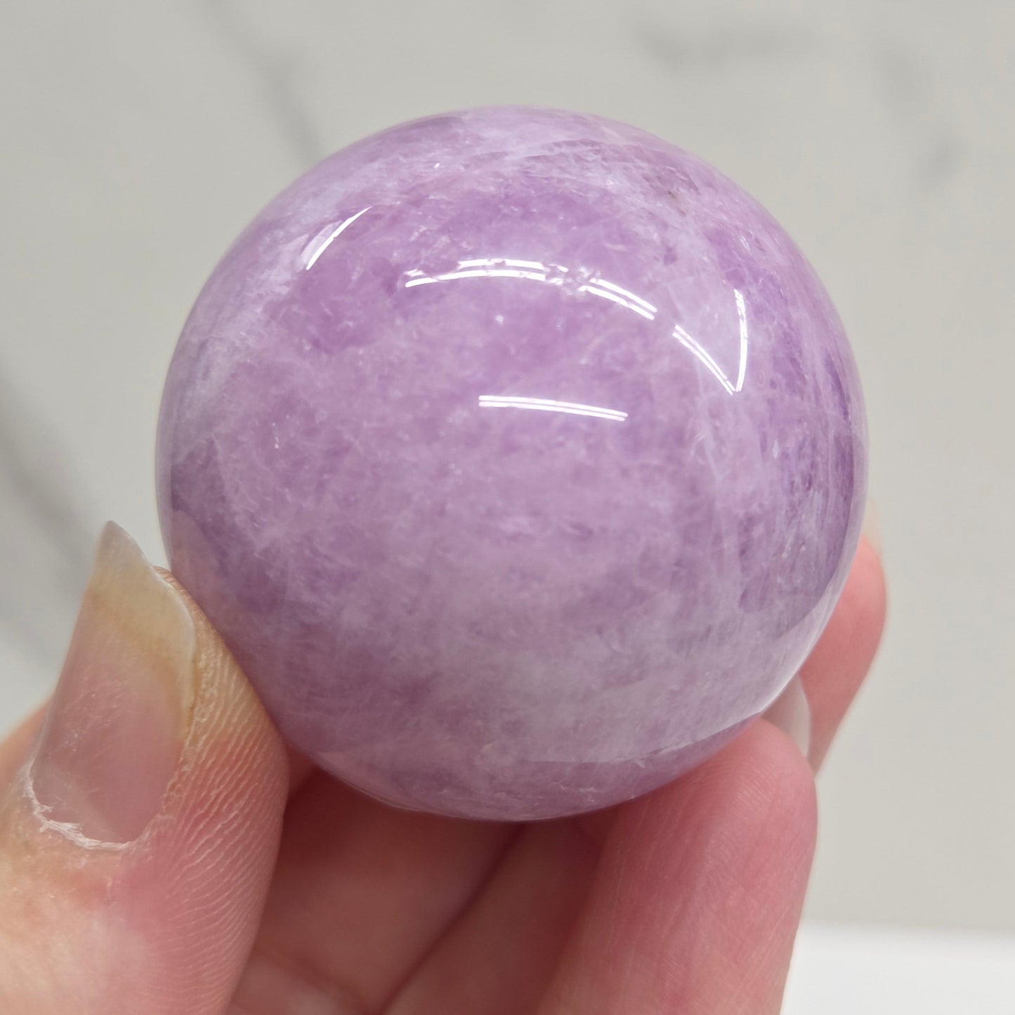 Hand holding a purple and white crystal sphere against a neutral background