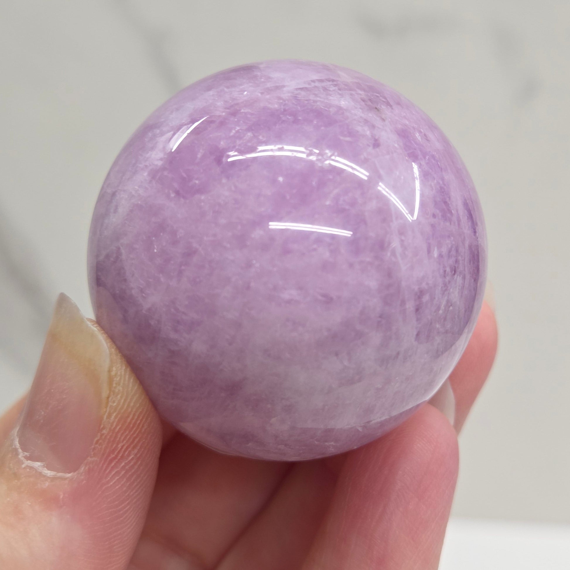Hand holding a purple and white crystal sphere against a neutral background