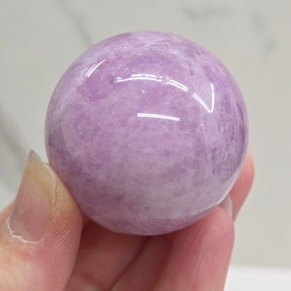 Hand holding a purple and white crystal sphere against a neutral background