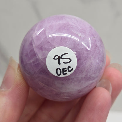 Hand holding a purple and white crystal sphere against a neutral background