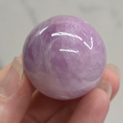 Hand holding a purple and white crystal sphere against a neutral background