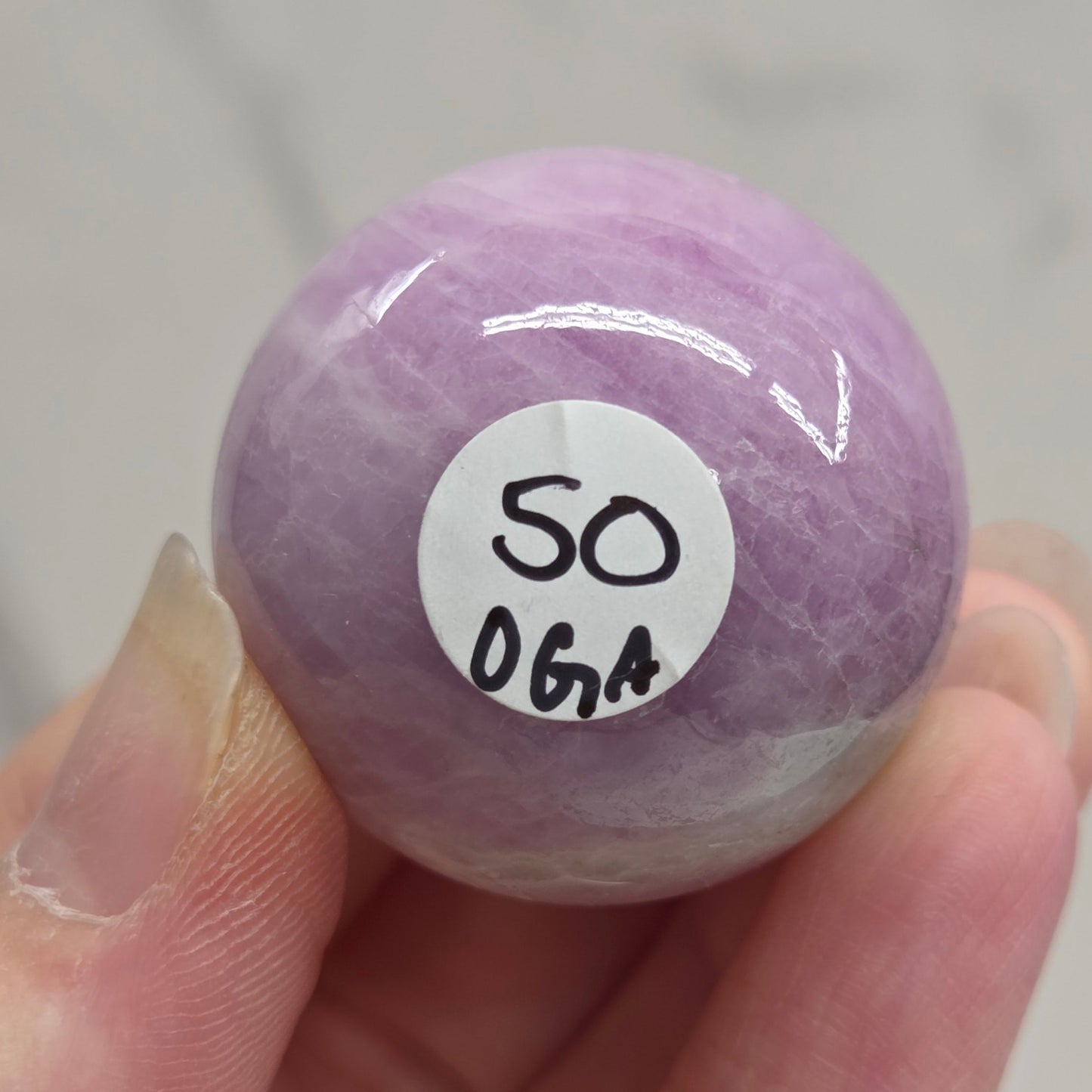 Hand holding a purple and white crystal sphere against a neutral background