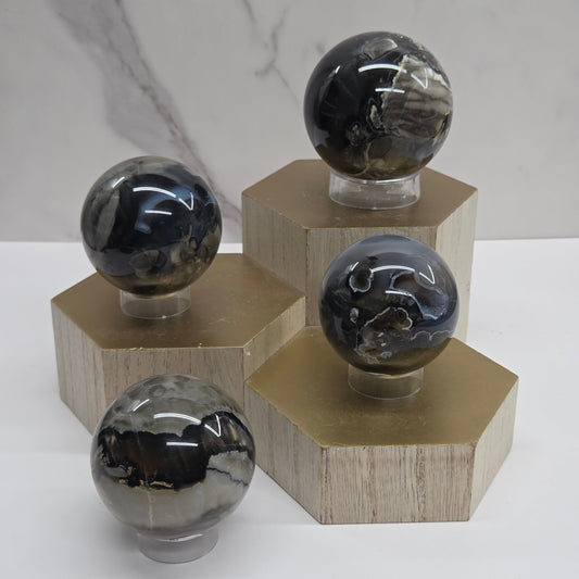 Brown and black crystal spheres on acrylic holders and a wooden stand against a neutral background