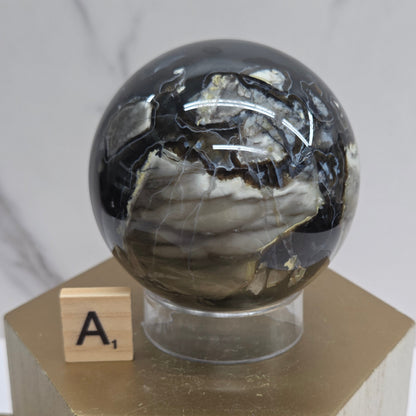 Brown and black crystal spheres on acrylic holders and a wooden stand against a neutral background
