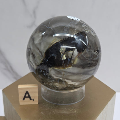 Brown and black crystal spheres on acrylic holders and a wooden stand against a neutral background