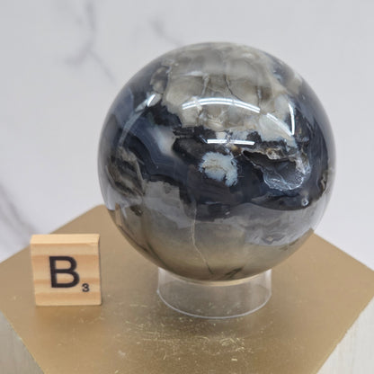 Brown and black crystal spheres on acrylic holders and a wooden stand against a neutral background