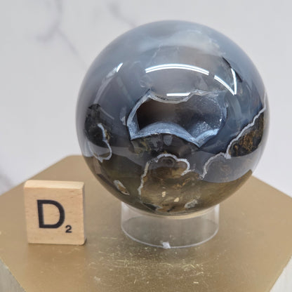 Brown and black crystal spheres on acrylic holders and a wooden stand against a neutral background
