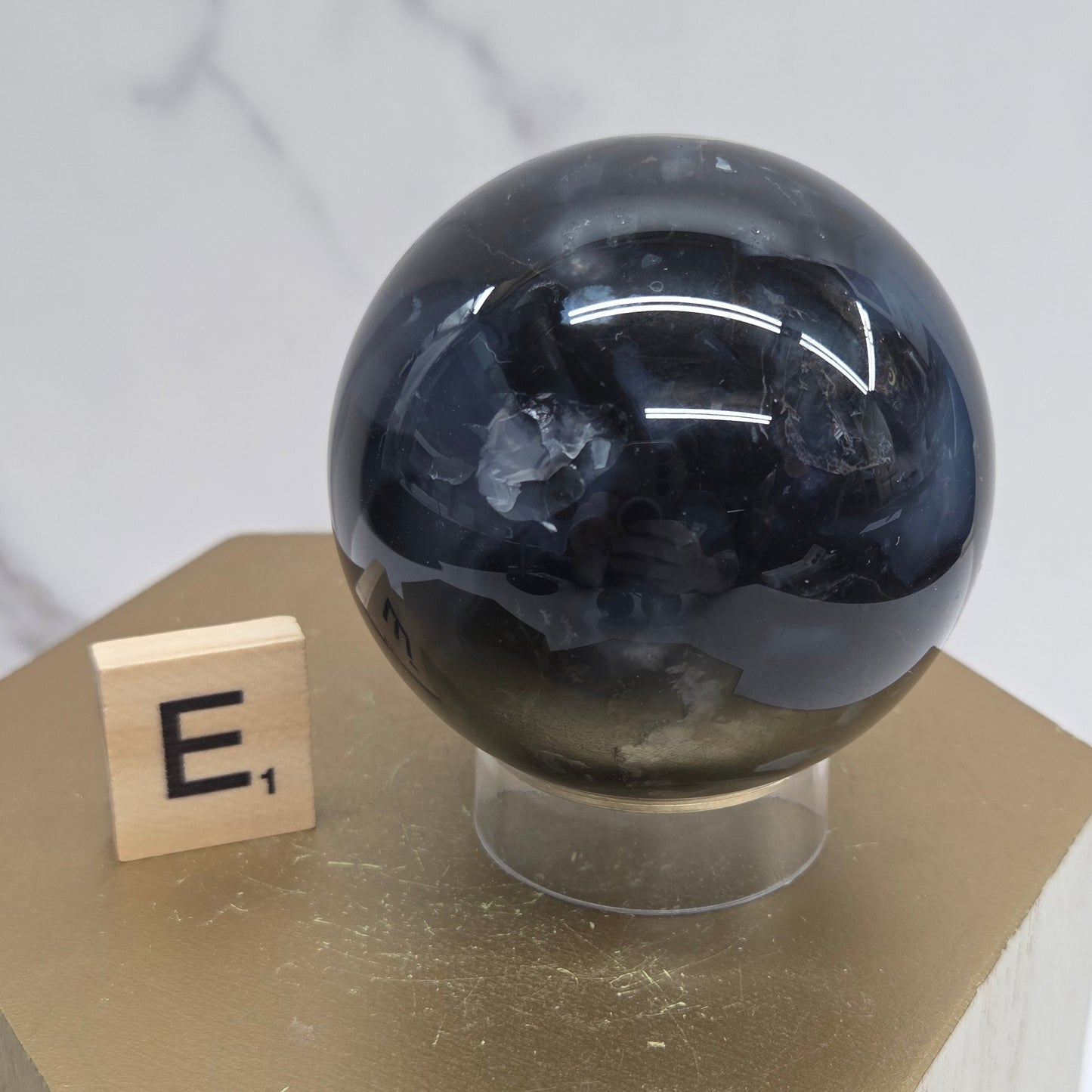 Brown and black crystal spheres on acrylic holders and a wooden stand against a neutral background