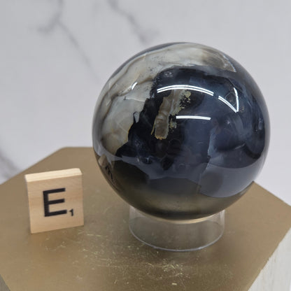 Brown and black crystal spheres on acrylic holders and a wooden stand against a neutral background