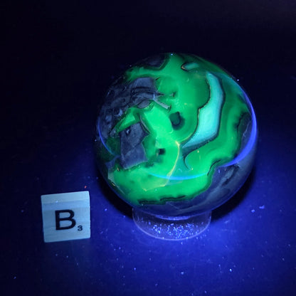 Brown and black crystal spheres on acrylic holder under UV light against a neutral background