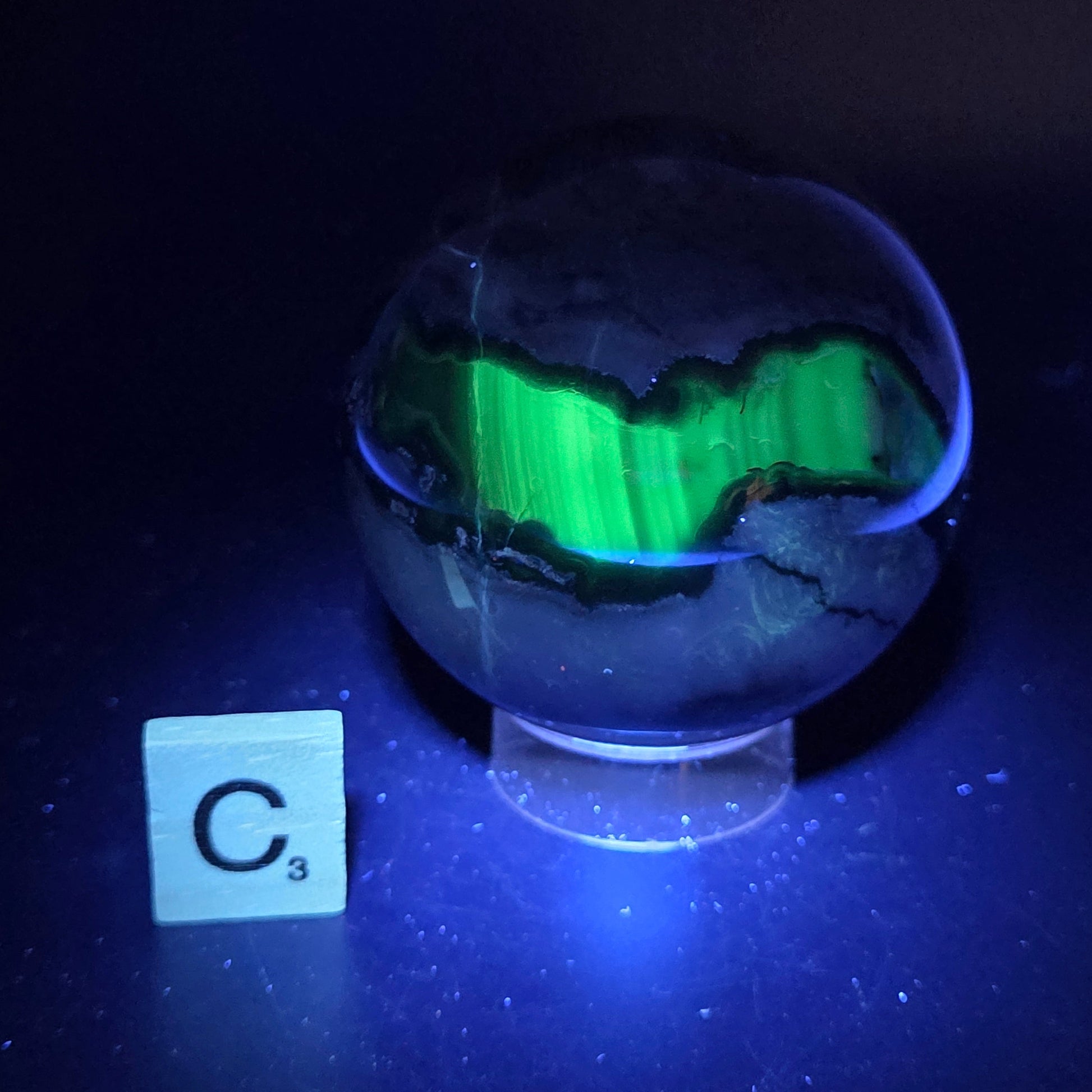 Brown and black crystal spheres on acrylic holder under UV light against a neutral background
