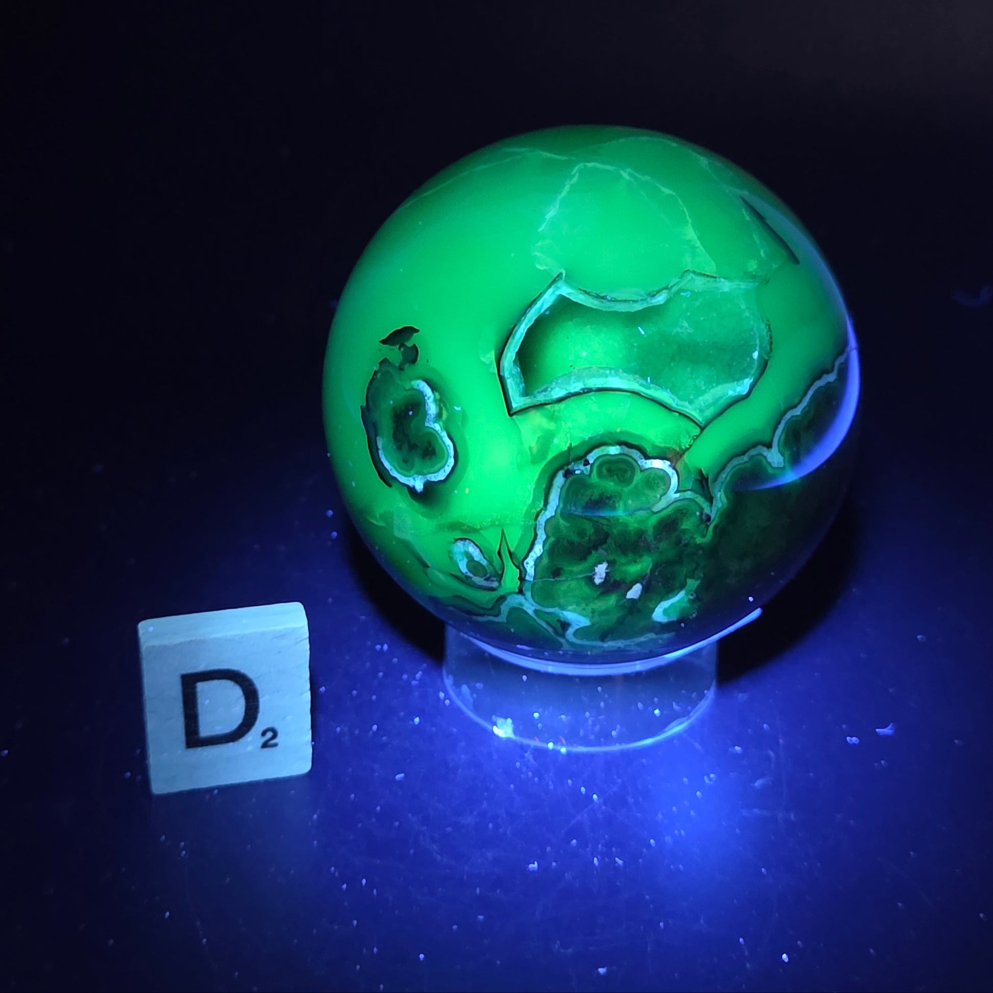 Brown and black crystal spheres on acrylic holder under UV light against a neutral background