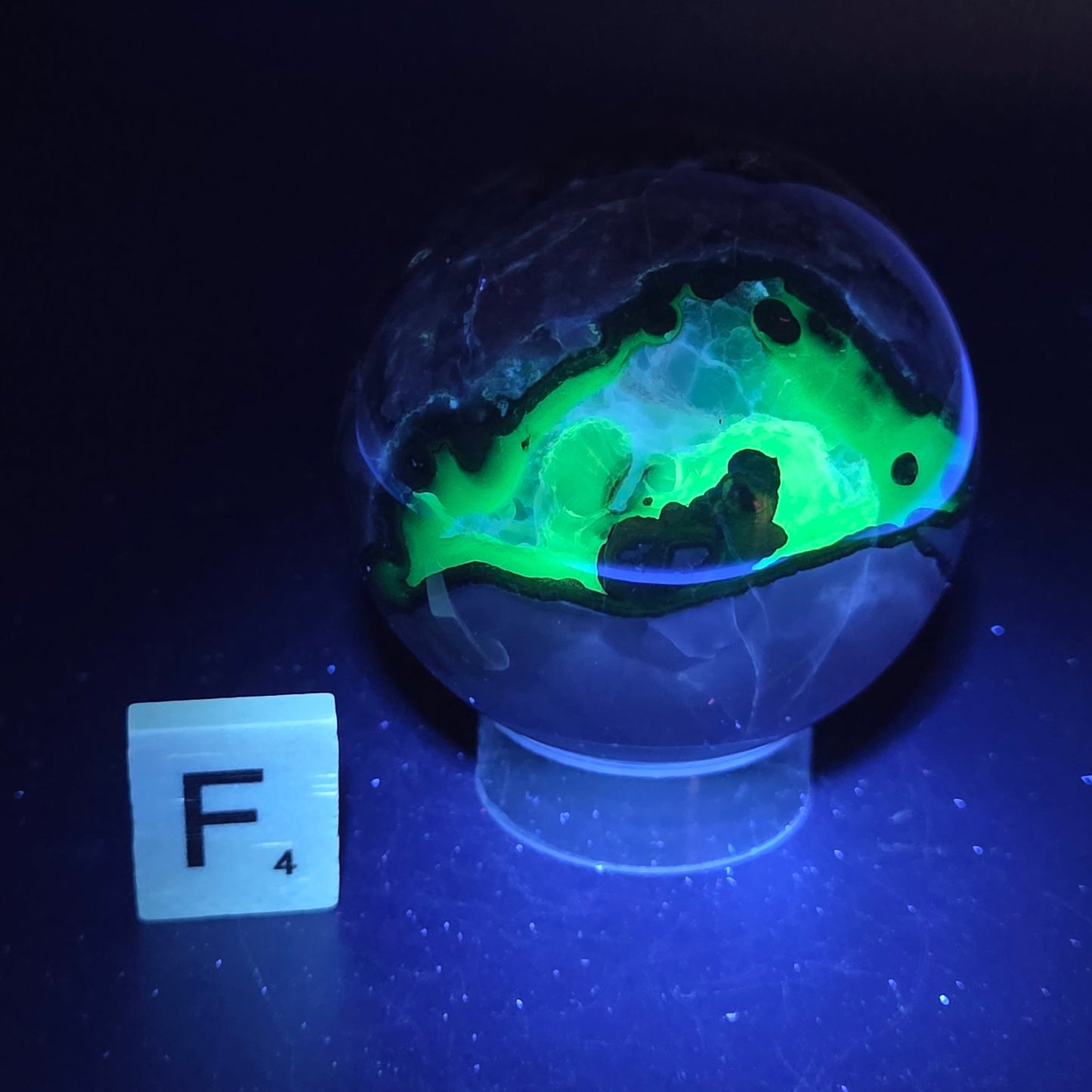 Brown and black crystal spheres on acrylic holder under UV light against a neutral background