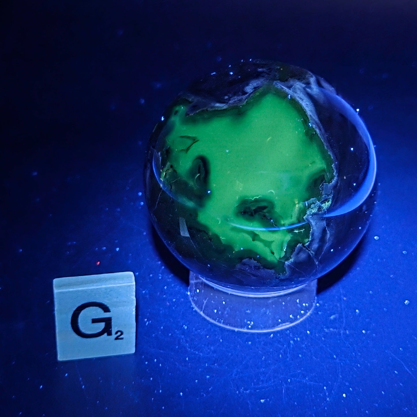 Brown and black crystal spheres on acrylic holder under UV light against a neutral background