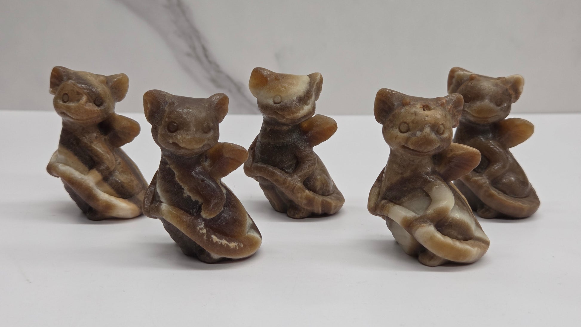 Five small brown dragon figurines on a white surface with a marble-patterned wall in the background.