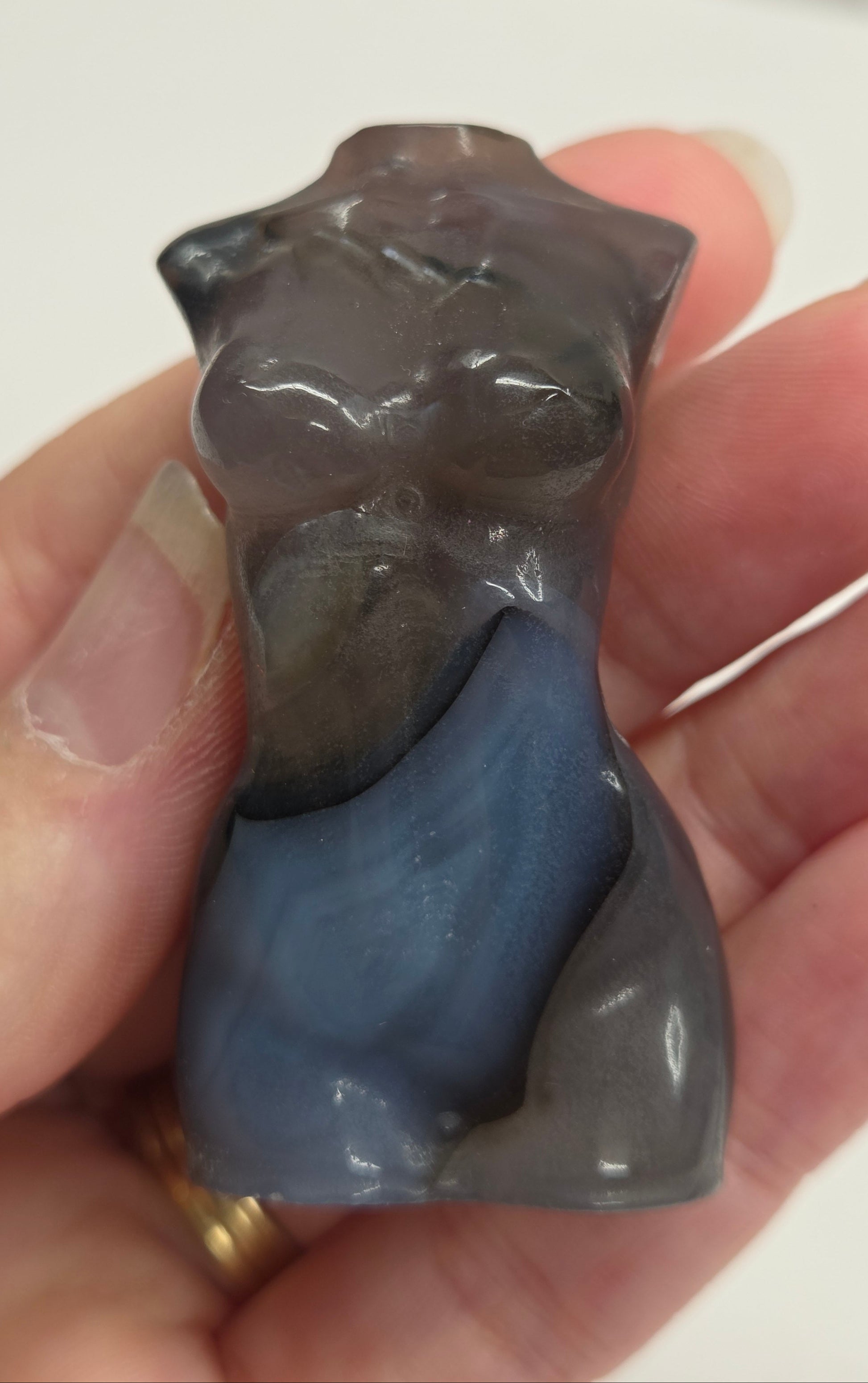 Hand holding a small blue and gray stone figurine against a plain background