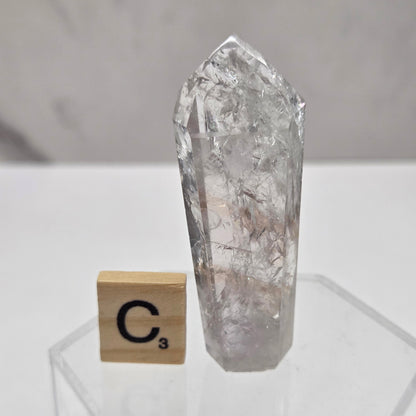 Clear crystal point on a white surface with a wooden block featuring a symbol.