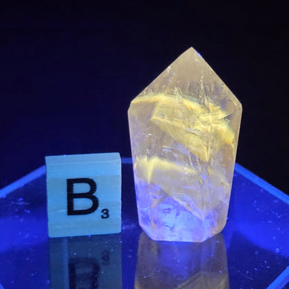 Crystal glowing under UV light on a reflective surface with a dark background