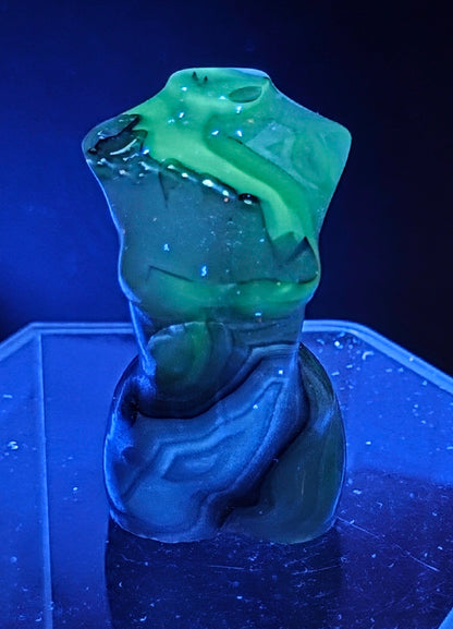 Gray stone sculpture of a woman's torso under UV light on a dark background