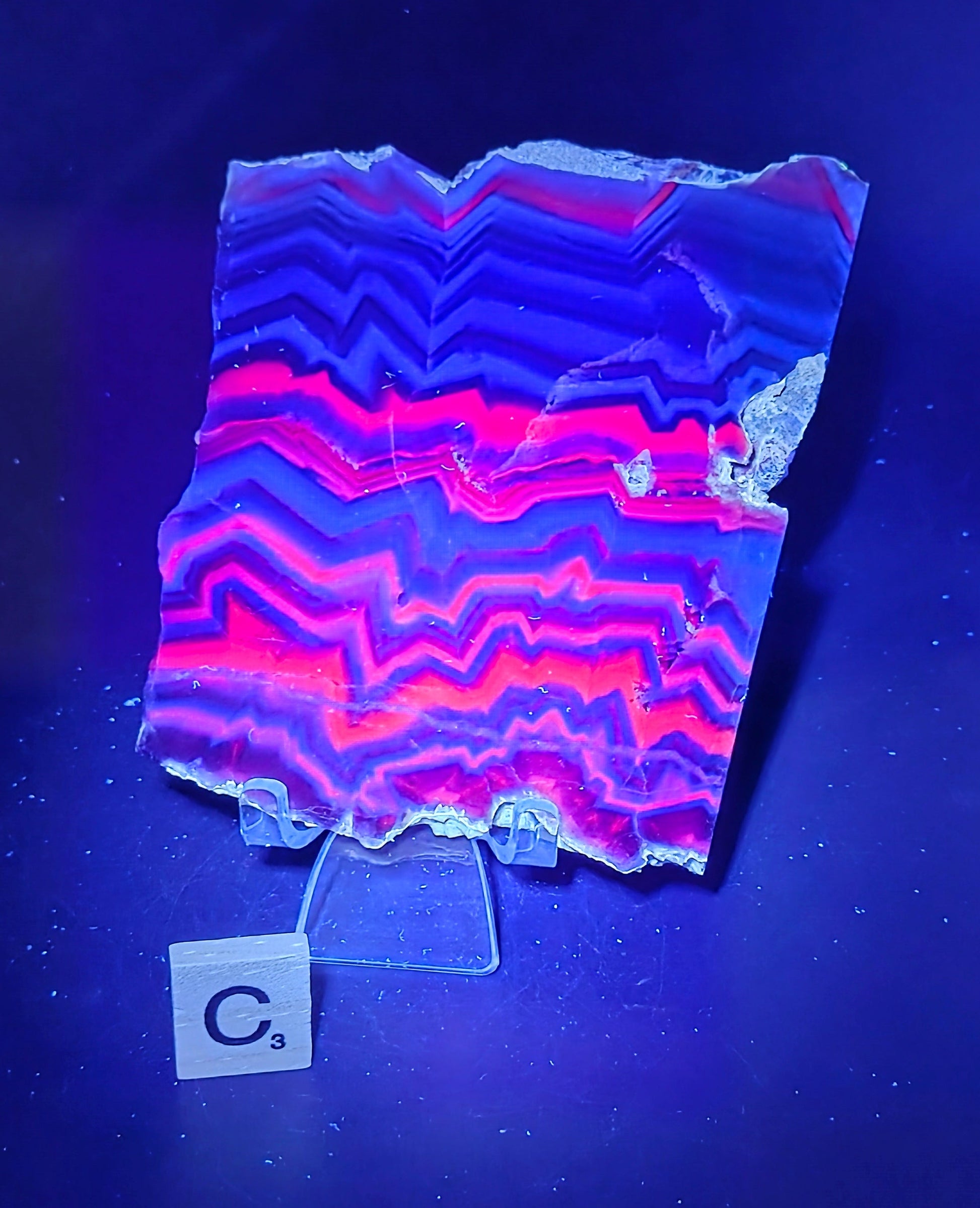 Banded fluorite slab under UV light on a stand against a neutral background